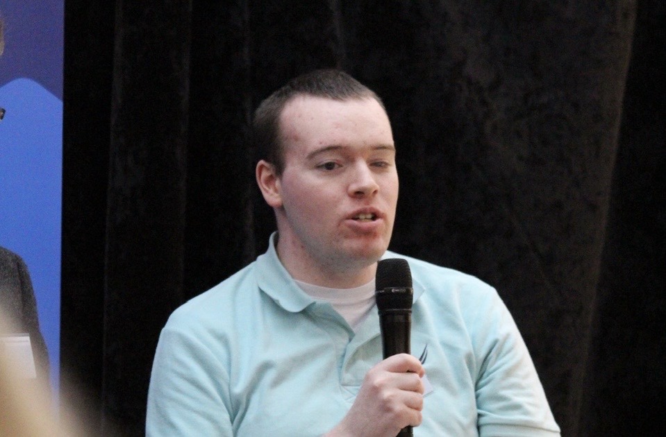 David Redmond holds a microphone and speaks on stage at the International Association of Accessibility professionals conference in Dublin. 